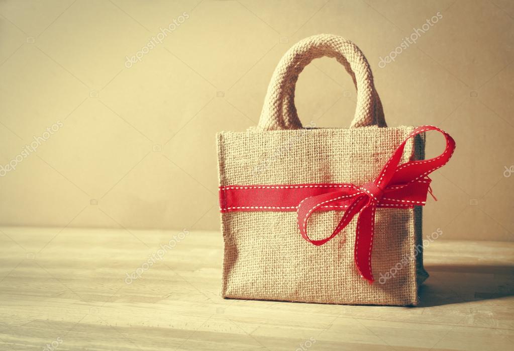 Beautiful gift bag with red bow on wood background and color filters