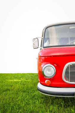 Yeşil çimlerin üzerine park etmiş eski kırmızı bir minibüsün temiz beyaz bir arka planı var. Minimalist seyahat ve macera konsepti, özgürlüğü sembolize ediyor, yolculuk yaşam tarzı, ve nostalji.