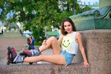 St. Petersburg 'da bir aslan heykelinin arka planında granit bir korkulukta oturan patenli genç bir kız.