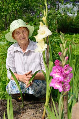 Bir yatakta beyaz ve mor kılıç çiçeği ile yaşlı bir kadın.