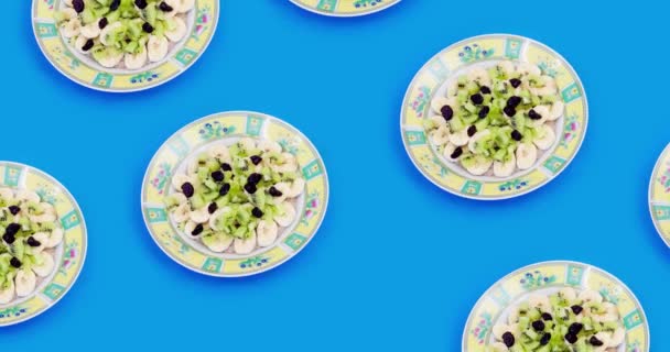 Sund morgenmad. Havre med banan og kiwi med et par tranebær i en skål. Muesli med skiftende baggrundsfarve, rød og blå. Set fra oven. – Stock-video