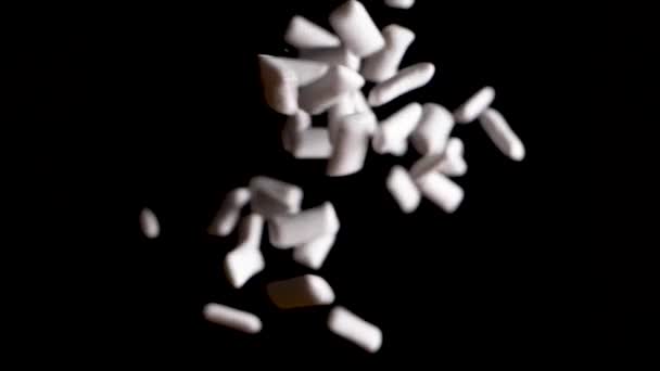 Witte kauwgom vallen van boven in een zwarte achtergrond in slow motion — Stockvideo