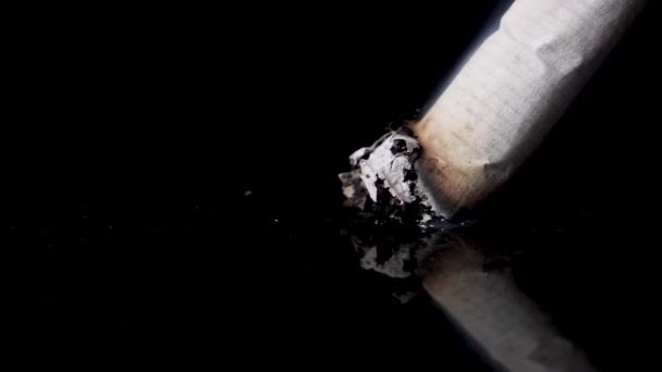 Släpper ut en cigarett på svart reflekterande yta, slow motion. — Stockvideo