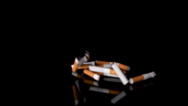 Házení kusů cigaret na černém reflexním pozadí z pravé strany. — Stock video