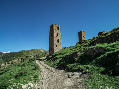 Dağıstan 'daki dağların zirvesindeki eski ortaçağ taş kulelerinin kalıntıları mavi gökyüzünün altındaki yeşil tarlalarda.