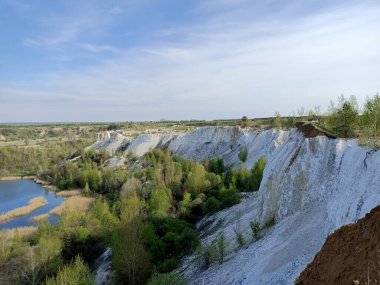 Tebeşir dağının beyaz yamacı. Ormanda göller var. Mavi gökyüzünün altında bulutlar var.