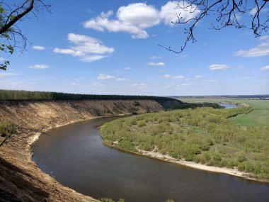 Riverbend in the deep forest with green trees around and under blue sky with clouds