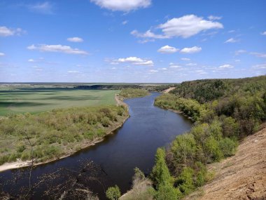 Riverbend in the deep forest with green trees around and under blue sky with clouds