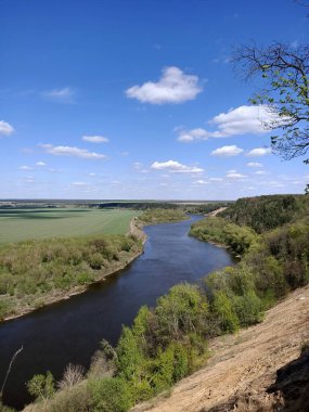 Riverbend in the deep forest with green trees around and under blue sky with clouds