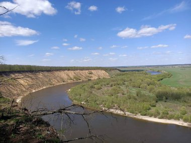 Riverbend in the deep forest with green trees around and under blue sky with clouds