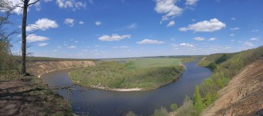 Riverbend in the deep forest with green trees around and under blue sky with clouds