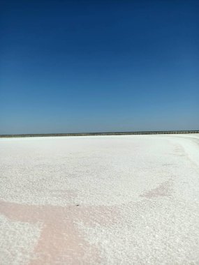 Layer of white salt on the pink rose salt lake under blue sky