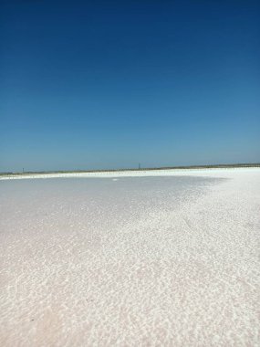 Layer of white salt on the pink rose salt lake under blue sky