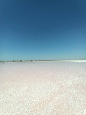 Layer of white salt on the pink rose salt lake under blue sky