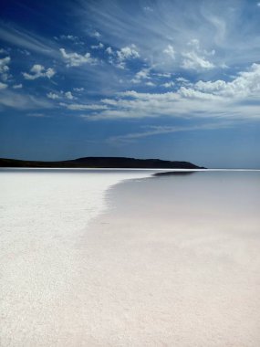 Layer of white salt on the pink rose salt lake under blue sky