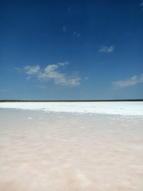 Layer of white salt on the pink rose salt lake under blue sky