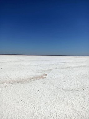 Layer of white salt on the pink rose salt lake under blue sky