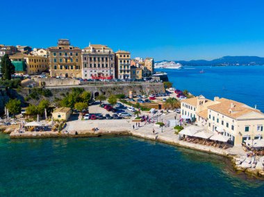 Yunanistan 'ın Korfu kasabasındaki tarihi rıhtım manzarası. Renkli binalar ve sahil kafeleri uzaktaki turkuaz İyon Denizi 'ne bakıyor.