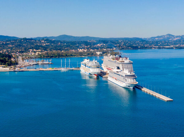 Вид с воздуха на главный порт Корфу, Греция, с двумя большими круизными кораблями, пристыкованными. Потрясающий средиземноморский пейзаж с голубыми водами и зелеными горами