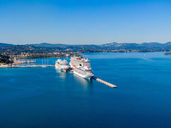 Вид с воздуха на главный порт Корфу, Греция, с двумя большими круизными кораблями, пристыкованными. Потрясающий средиземноморский пейзаж с голубыми водами и зелеными горами
