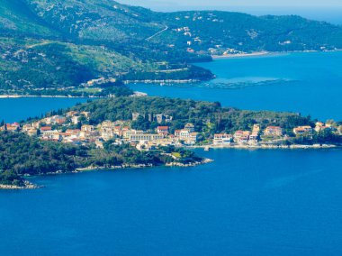 Yunan adası Corfu 'daki Kassiopi' nin sakin körfezinin havadan görünüşü, kıyıya kurulmuş büyüleyici köy ve canlı mavi suyu çevreleyen yemyeşil tepeler.
