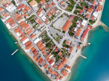 Yunanistan 'da geleneksel kırmızı kiremitli çatıları ve turkuaz turkuaz deniz manzaralı pitoresk bir kıyı köyünün insansız hava aracı görüntüsü