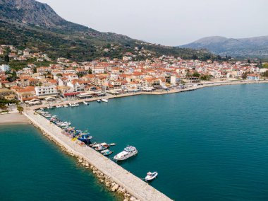 Astakos 'un havadan görünüşü, sakin bir limanı, tekneli uzun bir iskelesi ve bir dağın eteklerine kurulmuş kırmızı çatılı evleri olan resim gibi bir Yunan kıyı kasabası..