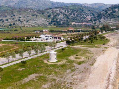 Sahilin kıyısındaki çimenli bir arazide eşsiz bir taş değirmeni. Arka planda dağlar, tarihin ve doğanın güzel bir harmanı..