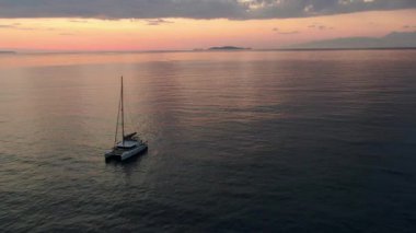 Serene Pembesi Günbatımında Açık İyon Denizi 'ne demirlenmiş lüks bir Katamaran Yelkenlisinin Hava Aracı Çekimi