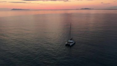 Güzel Pembe ve Turuncu Günbatımında Sakin Denizde Çapalanmış Yalnız Bir Katamaran Yelkenlisinin Hava Görüntüsü