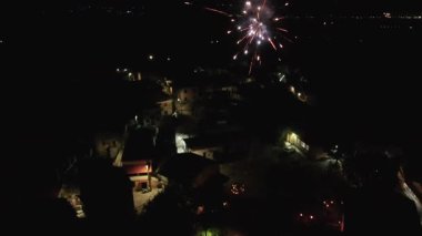 Havai fişeklerin hava aracı görüntüsü bir kutlama sırasında küçük, karanlık bir köyde patlıyor.