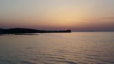 Sakin İyon Denizi 'nden uçakla Acharavi, Corfu, Yunanistan' ın siluetli sahillerine doğru uçarken güneş uzak burnun ardından batıyor.