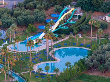 Lüks bir Akdeniz tatil beldesi için çarpıcı bir hava aracı perspektifi. Canlı bir su parkı, dingin yüzme havuzları, dinlenme yerleri, palmiye ağaçları ve seçkin villalar yer alıyor. Yaz tatili kavramı.