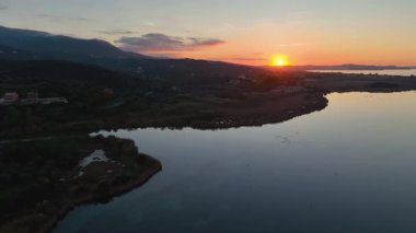 Korission Gölü ve Yunanistan 'ın Korfu kentindeki İyon Denizi üzerinde çarpıcı bir altın gün batımının yüksek hava aracı görüntüsü. Sakin su gökyüzünü yansıtır.