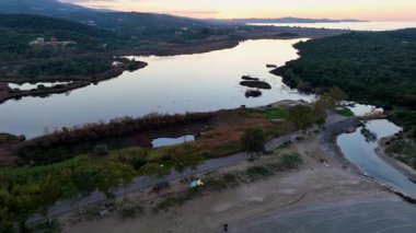 Kumlu plajın üzerinden geçen hava aracı videosu ve akşam karanlığında Korission Gölü 'nü denize bağlayan halat. Korfu, Yunanistan, günbatımı