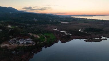 Antinioti Gölü 'nün kıyısındaki lüks bir villa ve zeytin ağaçlarının üzerinde uçan hava aracı videosu, Korfu, Yunanistan, güzel bir günbatımında