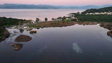Antinioti Gölü 'nün üzerinden Yunanistan' ın Korfu sahiline doğru uçan hava aracı videosu, pembe alacakaranlıktaki sakin sulak alanları ve köyü yakalıyor.