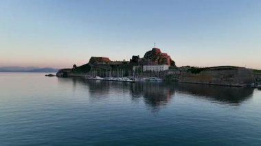 Güneş doğarken eski Corfu Kalesi 'ne (Palaio Frourio) ve yatlı Mandraki limanına doğru uçan güzel hava aracı görüntüleri.