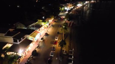 Ipsos 'un, Korfu' nun, Yunanistan 'ın gece hava aracı görüntüsü. Trafik, gece hayatı, sahil restoranları ve palmiye ağaçlarıyla dolu işlek sahil yolunda uçuyor..