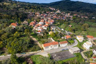 Korfu Yunanistan 'ın geleneksel Pagi köyünün yeşil tepeler ve zeytinlikleriyle çevrili kırmızı çatı evleri ve yerel bir basketbol sahası manzarası