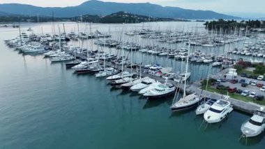 Akdeniz 'de alacakaranlıkta yelkenli ve direklerle dolu büyük yat marinasının panoramik hava manzarası, arka planda dağlar