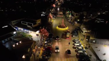 Noel ağacının dolambaçlı yolda olduğu ve trafik arabalarının tatil süslemeleri ile yolda ilerlediği, neşeli şehir caddesinin gece drone görüntüsü.