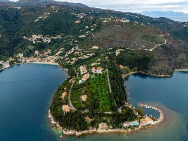 Yunanistan 'ın Corfu kentindeki yemyeşil Kouloura yarımadası ve Kalami körfezinin panoramik hava manzarası, lüks villalarla süslenmiş ve mavi İyon Denizi ile çevrili.