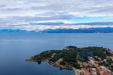 Kassiopi Yarımadası 'nın manzaralı deniz manzarası Korfu' nun arka planında dağlarla birlikte derin mavi İyon Denizi 'ne doğru ilerliyor.