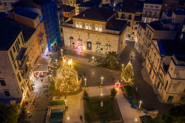 Geceleyin Korfu Şehir Meydanı 'nda aydınlatılmış Noel ağacı ve Yunanistan' da kemerli camlar ve sıcak tatil ışıklarının yer aldığı tarihi San Giacomo binasıyla