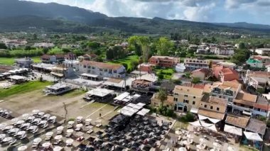 Roda Kuzey Korfu Yunanistan 'da turkuaz deniz ve yaz tatili konseptinin yanındaki kumlu sahilde renkli şemsiyeler ve güneşli yataklar bulunan plaj barları ve restoranların tepeden aşağı insansız hava aracı manzarası
