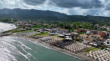 Roda sahil kasabasının panoramik hava aracı görüntüsü ve Kuzey Korfu Yunanistan 'daki kumlu plajda yaz tatili sezonu boyunca otel ve tatil beldeleri ve yeşil dağlar yer alıyor