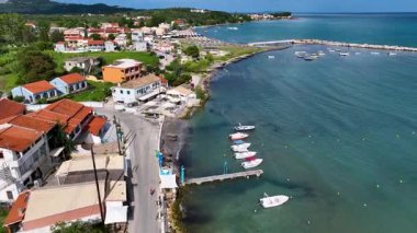 Kuzey Korfu Yunanistan 'da kıyı yolu ve küçük balıkçı iskelesinin hava araçları sürüyordu ve tekneler yaz günbatımında açık mavi sulara demirlemişti.