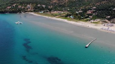 Kuzey Korfu Yunanistan 'ın güzel kumlu sahil şeridinin insansız hava aracı görüntüsü açık sığ su yatakları ve güneşli bir yaz gününde kumsalda uzun bir ahşap iskele.