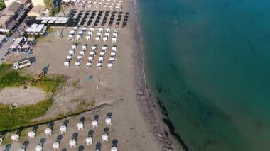 Roda Plajı Korfu Yunanistan 'ı çevreleyen sakin denizin üzerinde sakin bir hava akımı, güneşli bir öğleden sonra arka planda tatil otelleri ve yeşil tepelerle kıyıya bakıyor.